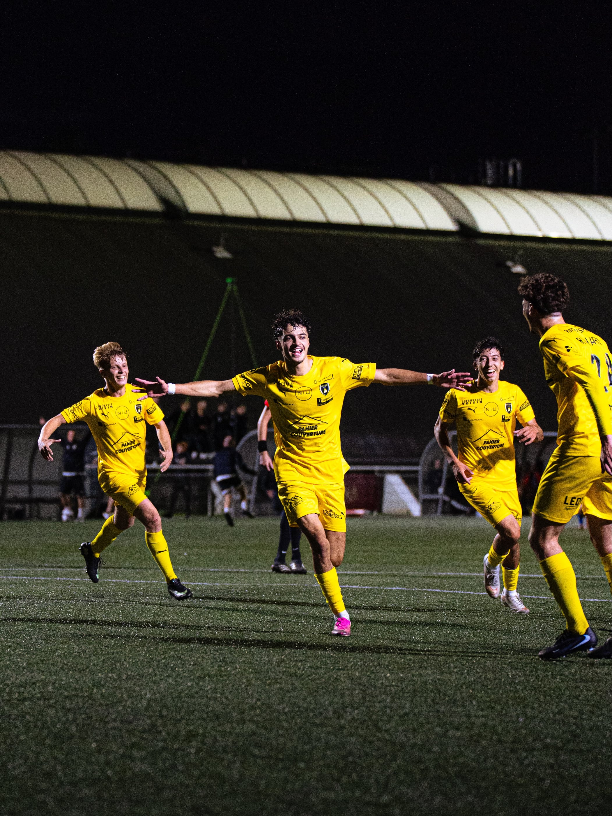Les joueurs de l'ASPTT Caen, en maillot jaune, courent fêter le but de la victoire contre Milizac sous les projecteurs